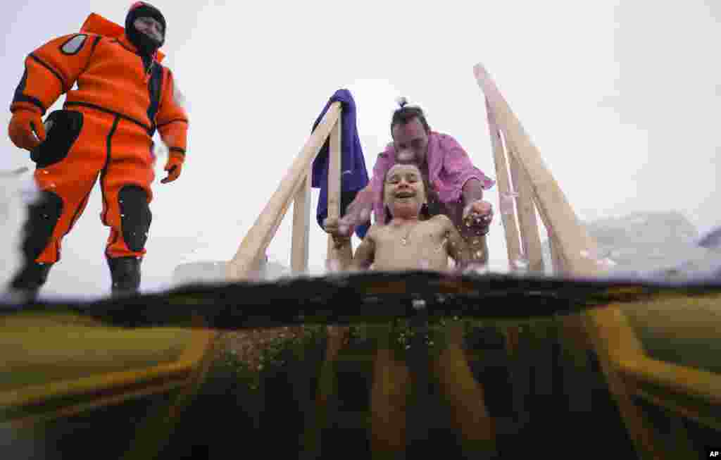 A rescue worker observes Russian Orthodox believer dipping his daughter in the icy water during a traditional Epiphany celebration in St.Petersburg, Russia.