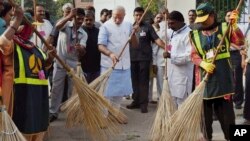 Indian Prime Minister Narendra Modi, center, sweeps an a road with a broom along with civic workers in New Delhi, India, Thursday, Oct. 2, 2014. (AP Photo/Press Trust of India)