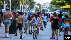 (FILES) In this file photo taken on June 26, 2020 a man rides a bicycle as people walk on Ocean Drive in Miami Beach, Florida