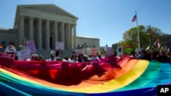 Demonstrators stand in front of a rainbow flag of the Supreme Court in Washington, Tuesday, April 28, 2015. 