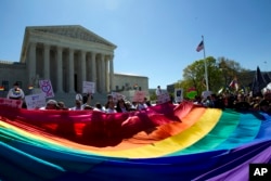 FILE - Demonstrators stand in front of a rainbow flag of the Supreme Court in Washington, D.C., April 28, 2015.