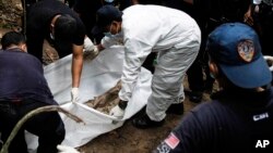 Malaysian police forensic team members excavate an unmarked grave in Wang Burma at the Malaysia-Thailand border outside Wang Kelian, Malaysia, May 26, 2015. 