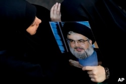 FILE -A woman covers her face with a picture of Hezbollah leader Sayyed Hassan Nasrallah at the funeral of a Hezbollah fighter who was killed by Israeli shelling, in the southern Beirut suburb of Dahiyeh, Lebanon, November 6, 2023.