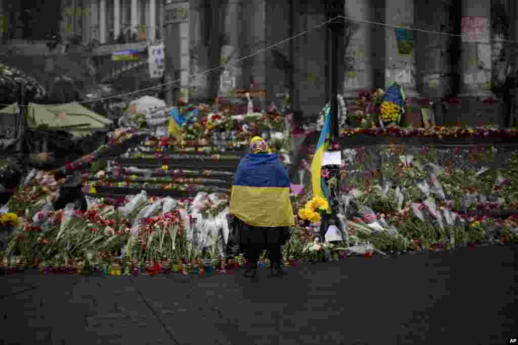 Seorang perempuan memakai bendera Ukraina di tempat penghormatan bagi para korban tewas dalam bentrokan dengan polisi di alun-alun Kemerdekaan di Kyiv (3/3). (AP/Emilio Morenatti)