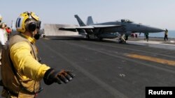 Flight deck crew member confirms the deck is all clear before a F/A-18C Hornet of Strike Fighter Squadron (VFA-87) take offs the aircraft carrier USS George H.W. Bush (CVN 77), in the Gulf August 12, 2014. 