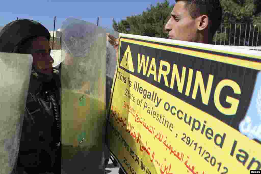 A Palestinian protester (R) holds a placard in front of an Israeli soldier during a demonstration in the West Bank village of al-Masara near Bethlehem, November 30.