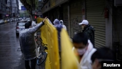 Workers wearing face masks repair barriers built up to block buildings from a street in Wuhan, Hubei province, the epicenter of China's coronavirus disease (COVID-19) outbreak.