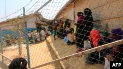 FILE - In this March 24, 2020, photo, Rohingya refugees wait in a relief distribution point at a refugee camp in Bangladesh.