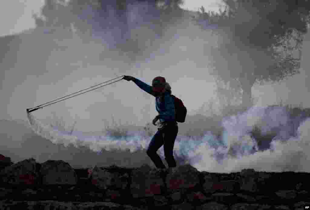 A Palestinian uses a slingshot to throws back a tear gas canister that was fired by Israeli troops during clashes with Israeli soldiers, outside the Ofer military prison, near the West Bank city of Ramallah.