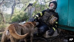 Seorang petugas pemadam kebakaran mengelus seekor anjing sambil beristirahat setelah memadamkan api di sebuah rumah pribadi yang terkena serangan udara Rusia di Kharkiv, Ukraina, Jumat, 3 Mei 2024. (Foto: Yevhen Titov/AP Photo)