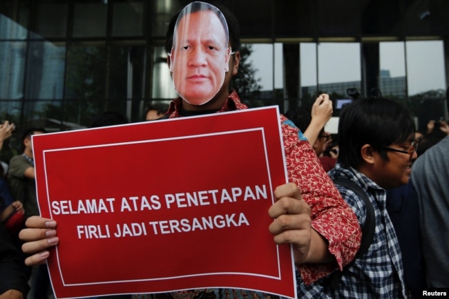 Seorang pria bertopeng bergambar Firli Bahuri, Ketua Komisi Pemberantasan Korupsi (KPK), membawa plakat bertuliskan "Selamat atas penetapan Firli sebagai tersangka" saat melakukan aksi di luar gedung KPK di Jakarta, 23 November 2023. (Foto: REUTERS/Ajeng Dinar Ulfiana)