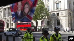Police officers walk past a flag hanging outside a coffee shop, depicting Britain's Prince William and Kate Middleton, on Whitehall, in central London April 27, 2011. Prince William will marry Kate Middleton at Westminster Abbey on April 29th. REUTER