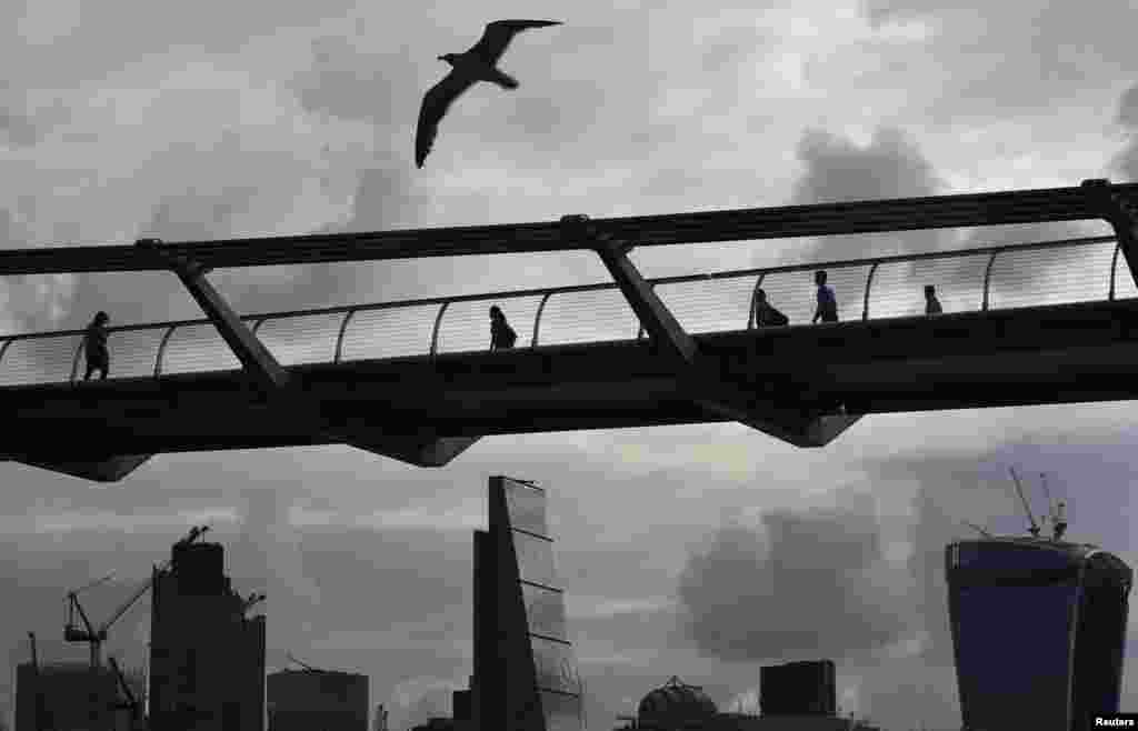 Workers cross the Millenium Bridge with the City of London seen behind, in London, Britain.