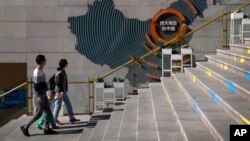 A family walks by a map showing Evergrande development projects in China at an Evergrande city plaza in Beijing, Sept. 21, 2021.