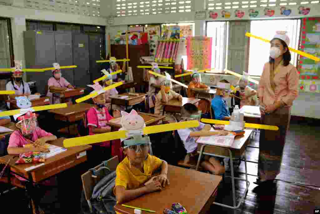 A teacher and students wearing hats designed for space keeper, practice social distancing to help curb the spread of the coronavirus at Ban Pa Muad School in Chiang Mai, north of Thailand.
