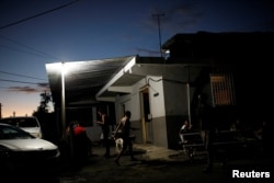 FILE - People gather to chat outside a mini-market that uses electricity from a generator, at the squatter community of Villa Hugo in Canovanas, Puerto Rico, December 12, 2017.