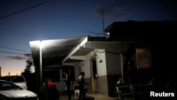 FILE - People gather to chat outside a mini-market that uses electricity from a generator, at the squatter community of Villa Hugo in Canovanas, Puerto Rico, December 12, 2017. 