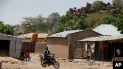 FILE - In this Monday, May 19, 2014 photo, an unidentified man rides a motorbike past houses in Chibok, Nigeria. Multiple suicide bombings have killed a number of civilians and a soldier and the toll is expected to rise among those critically wounded in the Chibok, community leaders said Thursday Jan. 28, 2016 in the town from which Boko Haram kidnapped scores of schoolgirls almost two years ago. 