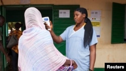 Seorang petugas kesehatan memeriksa suhu tubuh perempuan yang meninggalkan Guinea di perbatasan dengan Mali di Kouremale (2/10). (Reuters/Joe Penney)