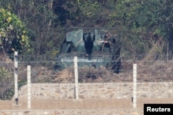 27일 한국 김포시의 전망대에서 바라본 남북 접경 지역에서 북한군 병사가 122mm 자주곡사포 위에 앉아 있다. 자주곡사포에는 "조선인민의 철천지원수 미제 침략자들을 때려부수자!"라는 구호가 적혀 있다.