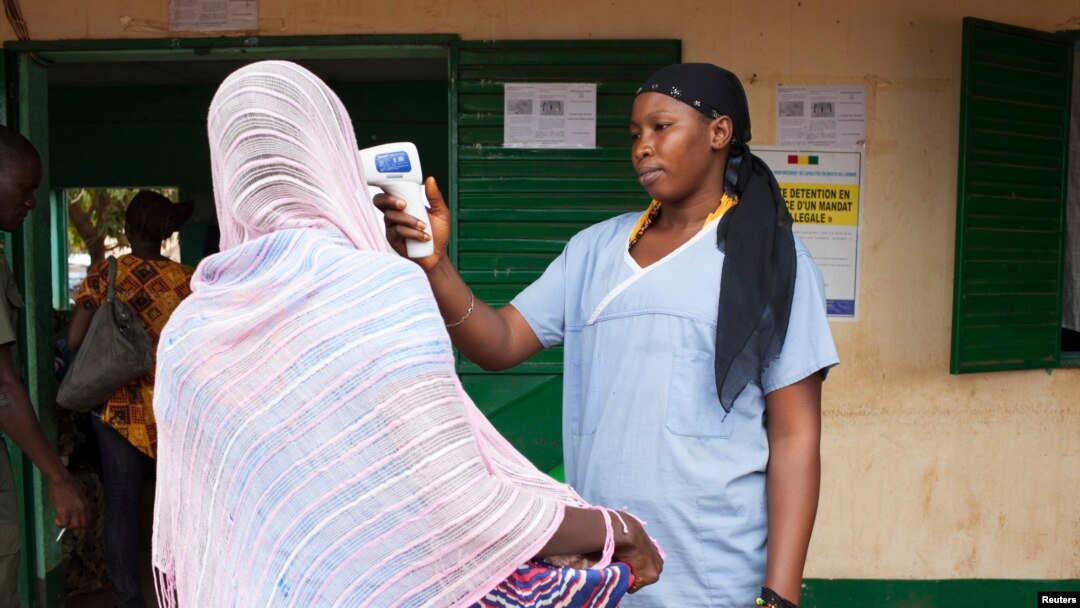 Seorang petugas medis memeriksa suhu searing perempuan yang meninggalkan Guinea di perbatasan Mali di Kouremale, 2 Oktober 2014.