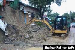 Rohingya refugees and others look on as machinery is used to remove debris after a landslide triggered by heavy rains in a camp at Ukhiya in Cox's Bazar district, Bangladesh, Tuesday, July 27, 2021
