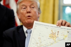 FILE - President Donald Trump holds up a map as he speaks about Harvey in the Oval Office of the White House, Sept. 1, 2017, in Washington.