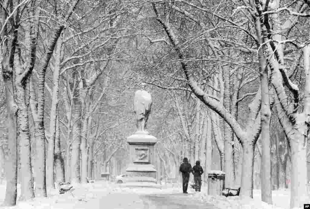 People walk along snow-covered Commonwealth Avenue Mall during a winter storm, in the Back Bay neighborhood of Boston, Massachusetts, March 14, 2017 .