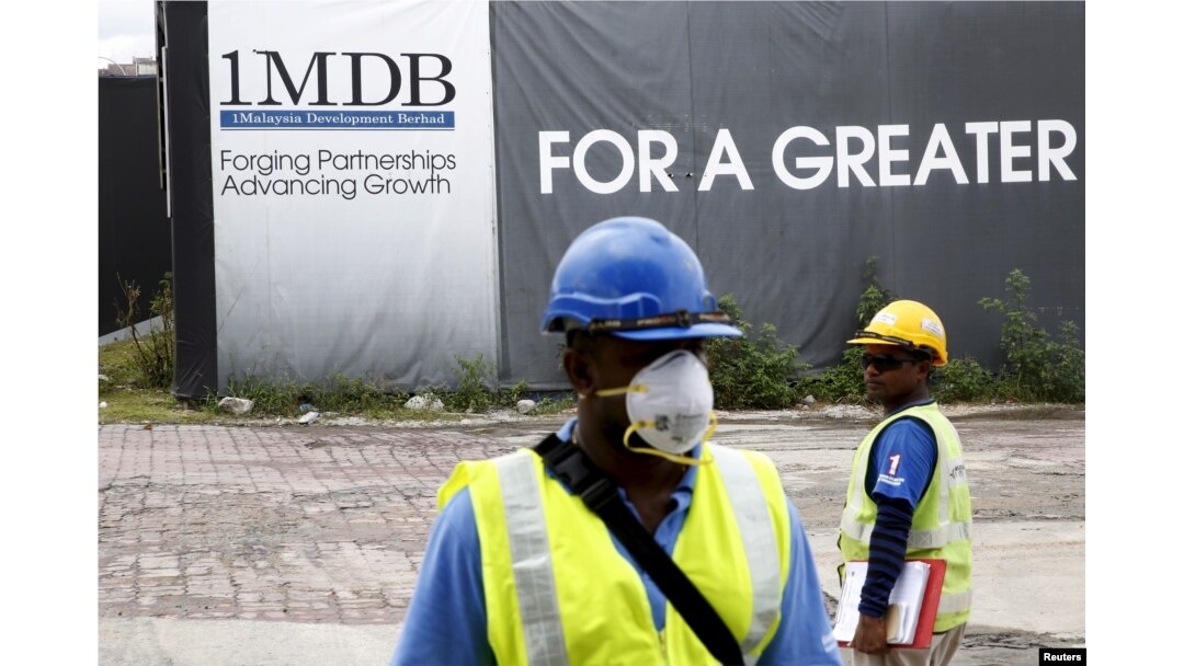 FILE - Construction workers stand in front of a 1Malaysia Development Berhad (1MDB) billboard at the Tun Razak Exchange development in Kuala Lumpur, Malaysia, Feb. 3, 2016.