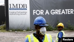 FILE - Construction workers stand in front of a 1Malaysia Development Berhad (1MDB) billboard at the Tun Razak Exchange development in Kuala Lumpur, Malaysia.