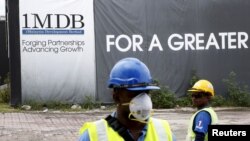 FILE - Construction workers stand in front of a 1Malaysia Development Berhad (1MDB) billboard at the Tun Razak Exchange development in Kuala Lumpur, Malaysia.