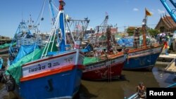 FILE - A fisherman sits as fishing vessels are seen docked after fishing operations stopped at a port in Samut Sakhon province, Thailand.