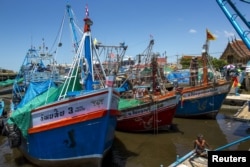 FILE - A fisherman sits as fishing vessels are seen docked after fishing operations stopped at a port in Samut Sakhon province, Thailand.