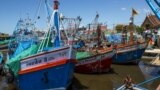 FILE - A fisherman sits as fishing vessels are seen docked after fishing operations stopped at a port in Samut Sakhon province, Thailand.