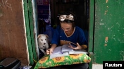 FILE - Annie Sabino, 16, a 9th-grader, completes her homework while tending to her family's sidewalk eatery beside their home, as schools remain closed during the COVID-19 outbreak, in Manila, Philippines, Jan. 6, 2021.
