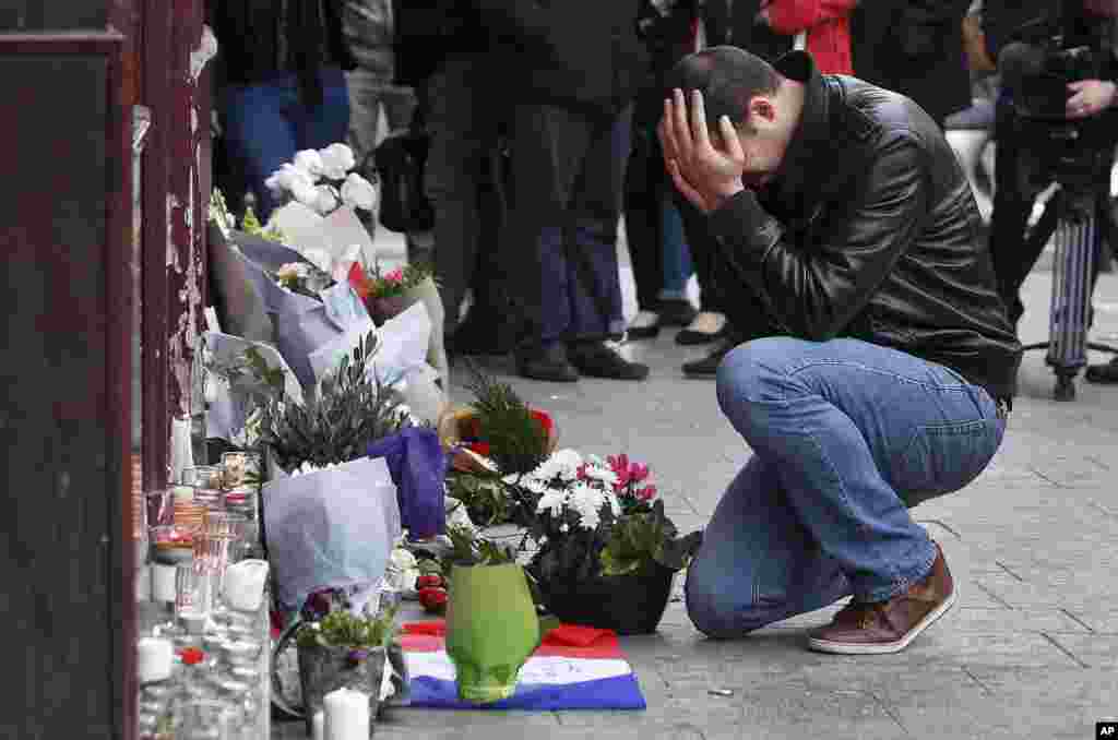 Wani mutumi ya rike kai a lokacin da yake ajiye furanni na jimami a kofar wani gidan abinci mai suna Carillon cafe, a Paris, Nov.14, 2015.