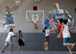 Boys plays beside images of former NBA basketball player Kobe Bryant at the "House of Kobe" basketball court in Valenzuela, north of Manila, Philippines on Monday, Jan. 27, 2020.