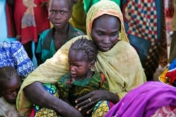 FILE - A mother and her child sit with other families at a camp for internally displaced people in Dougi, Cameroon, Oct. 24, 2013.