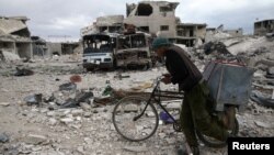 A man walks with his bicycle at a damaged site in the besieged town of Douma, Eastern Ghouta, in Damascus, Syria, March 30, 2018.