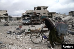 A man walks with his bicycle at a damaged site in the besieged town of Douma, Eastern Ghouta, in Damascus, Syria, March 30, 2018.