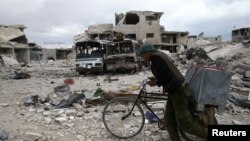 FILE - A man walks with his bicycle at a damaged site in the besieged town of Douma, Eastern Ghouta, near Damascus, Syria, March 30, 2018.