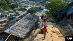 A Rohingya refugee boy (front) carries a chicken as he walks back to his makeshift house in Jamtoli refugee camp in Ukhia on December 11, 2019. (Photo by MUNIR UZ ZAMAN / AFP)