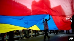 Un joven camina bajo una gran bandera venezolana durante un mitin organizado por trabajadores de la Compañía Nacional de Telecomunicaciones o CANTV para mostrar su apoyo al gobierno en Caracas, Venezuela. [Foto del 25 de fe]