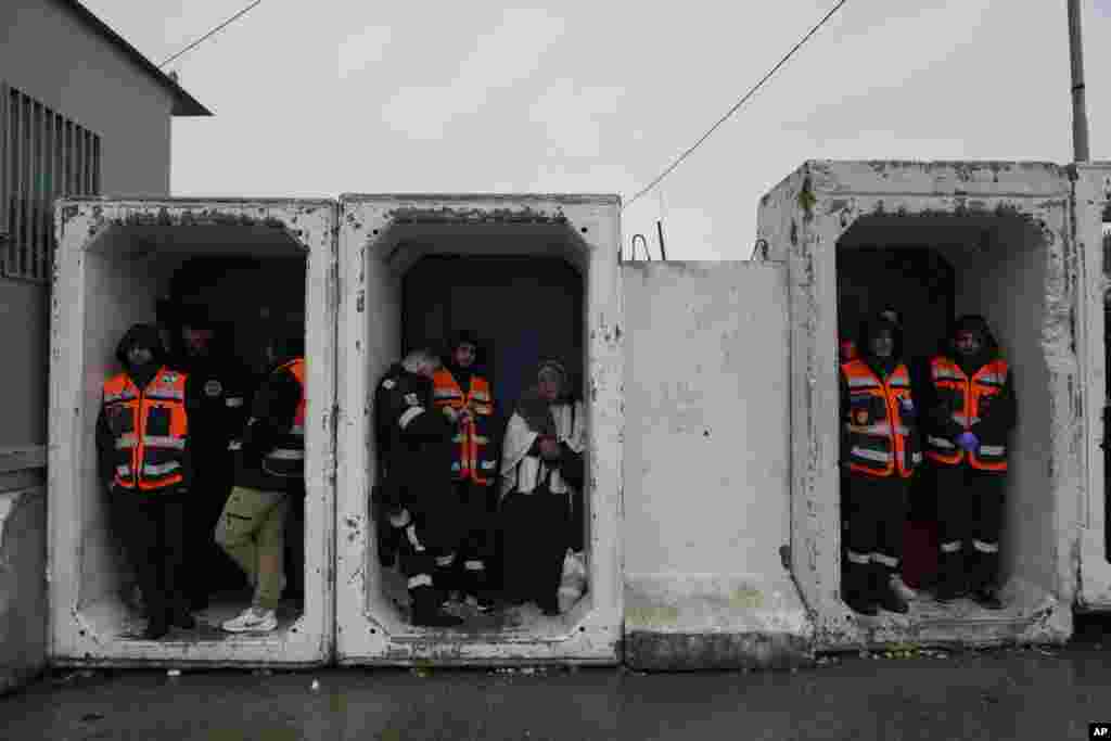 Petugas paramedis berlindung dari hujan sementara warga Palestina menyeberang dari pos pemeriksaan militer Israel Qalandia dekat kota Ramallah, Tepi Barat ke Yerusalem, untuk mengikuti salat Jumat di Masjid Al-Aqsa selama bulan suci Ramadan. (AP)&nbsp;