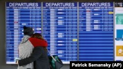 A man and woman embrace in front of a flight departures board at Dulles International Airport in Dulles, Va., Tuesday, March 17, 2020. (AP Photo/Patrick Semansky)