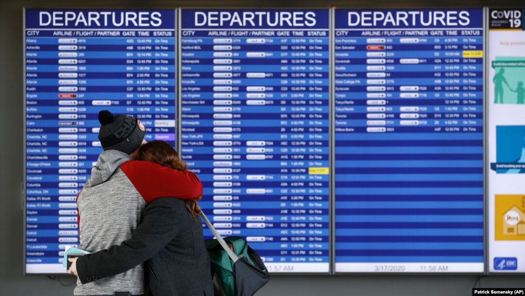 A man and woman embrace in front of a flight departures board at Dulles International Airport in Dulles, Va., Tuesday, March 17, 2020. (AP Photo/Patrick Semansky)