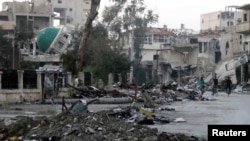 FILE - Men ride bicycles past a damaged mosque along a deserted street filled with debris in Deir al-Zor, Syria, March 5, 2014.