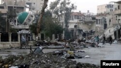 Men ride bicycles past a damaged mosque along a deserted street filled with debris in Deir al-Zor, Syria, March 5, 2014.