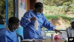 FILE: A health worker puts on her protective clothing before vaccinating people against Ebola at the hospital in the village of Kagando, near the border with Congo, in western Uganda. Taken June 15, 2019