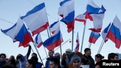 Spectators watch the action standing next to Russian and Crimean flags during celebrations marking the first anniversary of Russia's annexation of Ukraine's Black Sea peninsula of Crimea, in central Simferopol, March 16, 2015. 